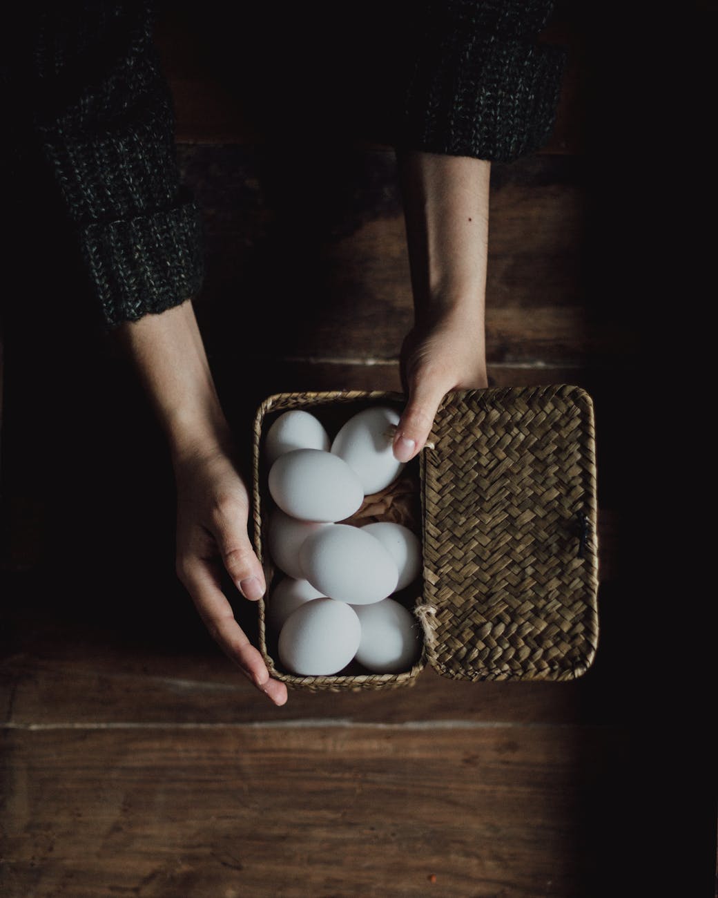 crop person holding chicken eggs in basket